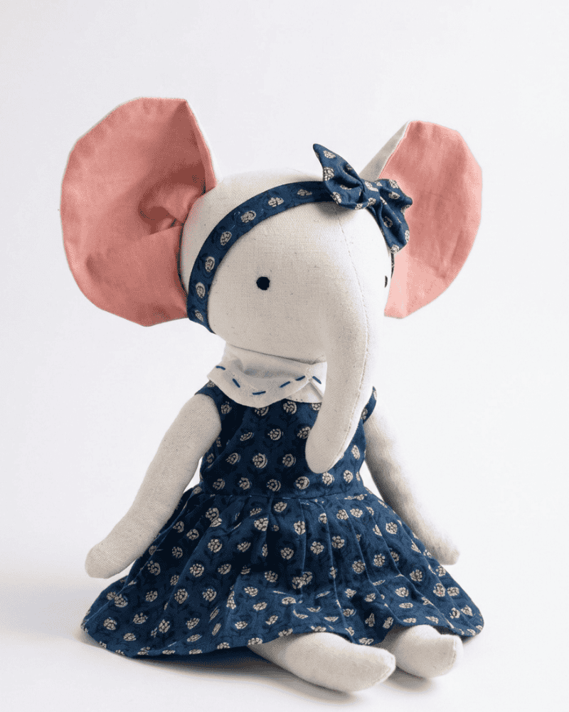 Stuffed elephant toy wearing a navy dress with white floral pattern and matching headband on a light gray background