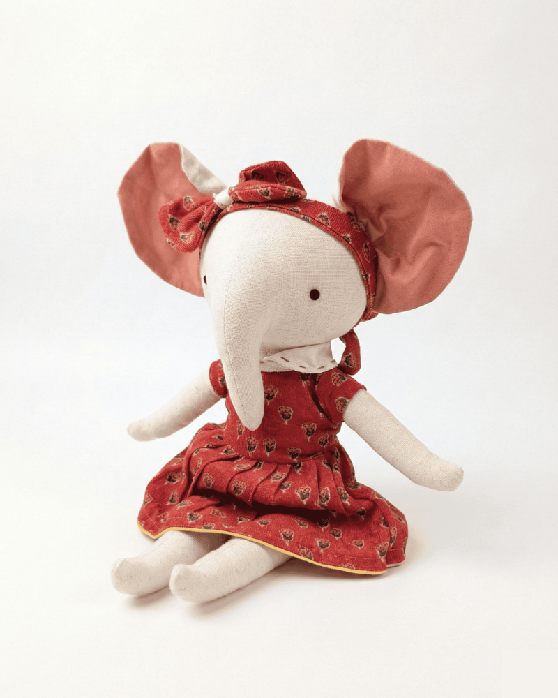 Stuffed elephant toy wearing a red dress and a red headband on a white background