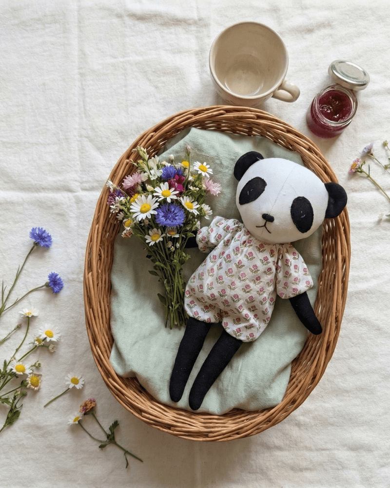 Wicker basket with a plush panda toy, flowers, and a mug on a light background
