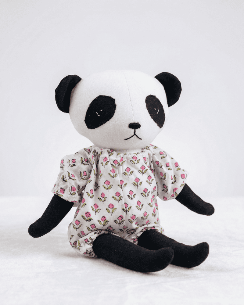 Panda soft toy wearing a floral dress on a white background