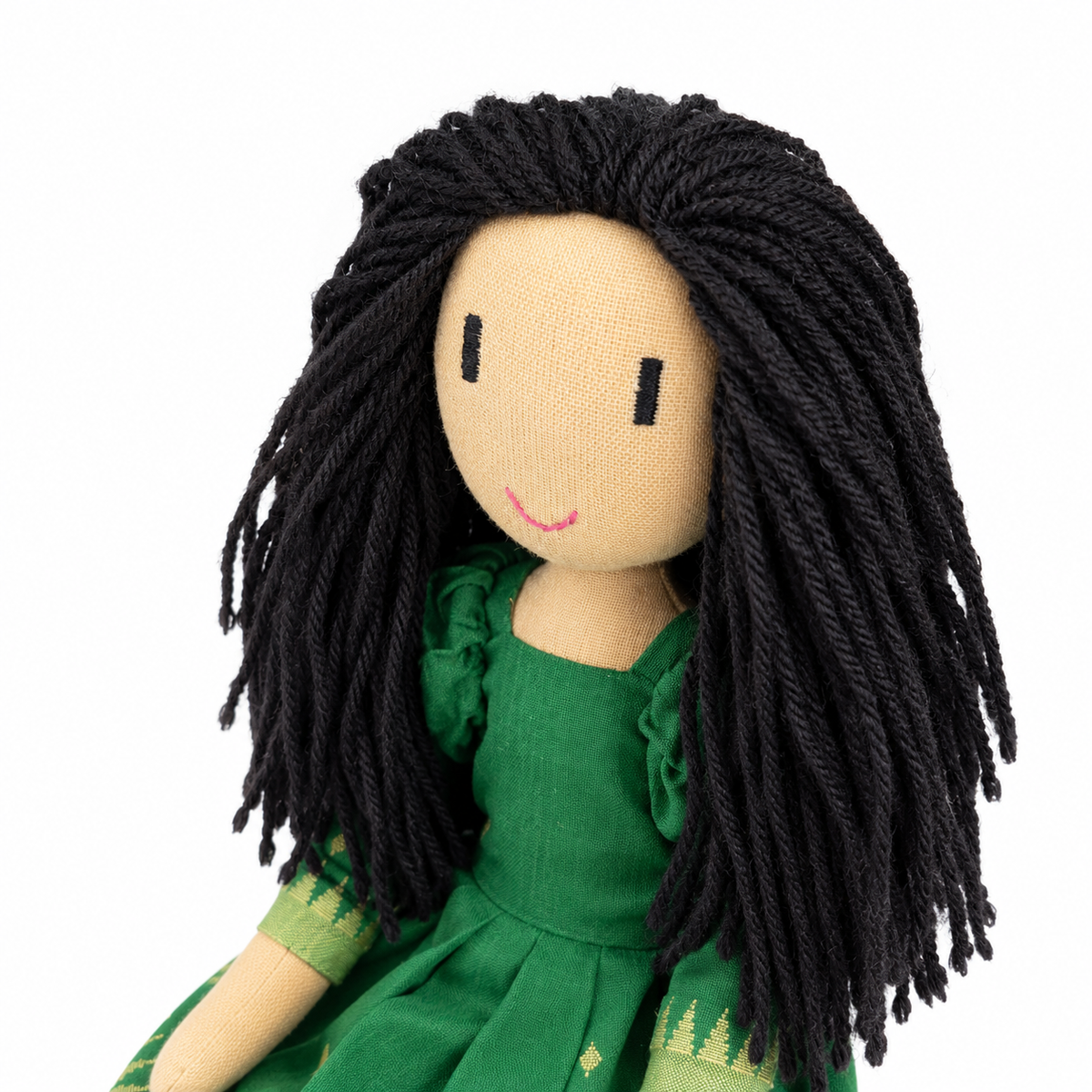 A handmade fabric doll 45 degrees shot with long black yarn hair, a beige linen face, and a green dress, shown against a plain white background.