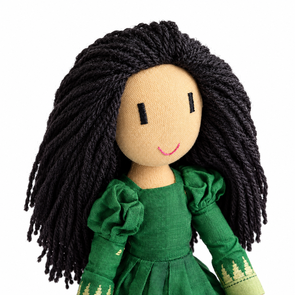 A handmade fabric doll with long black yarn hair, a beige soft cotton face, and a green dress, shown against a plain white background.