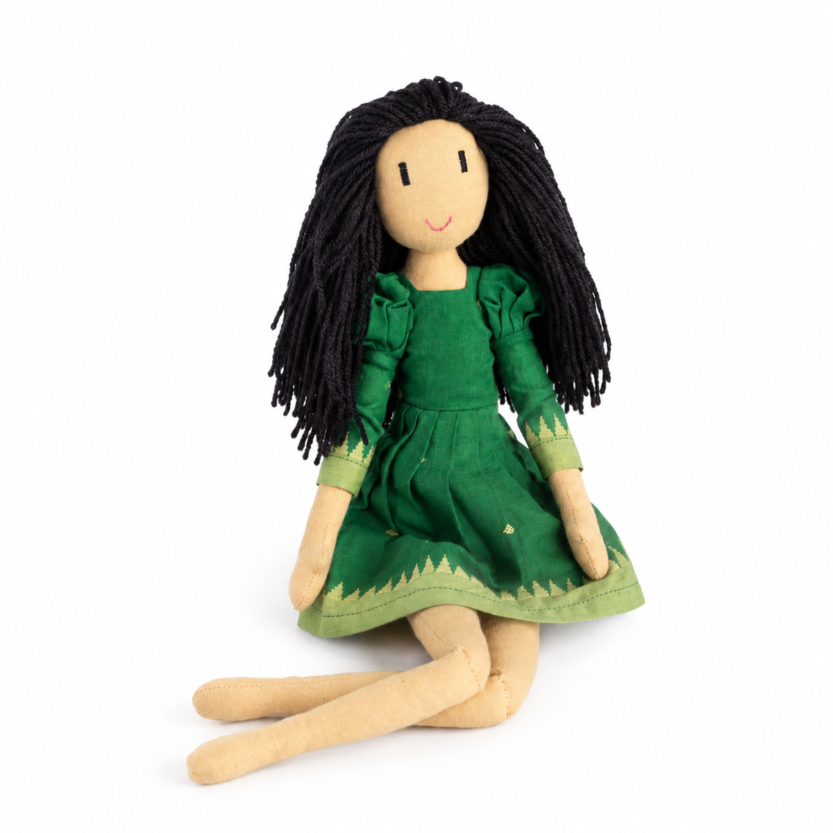 A handmade doll with long black yarn hair, wearing a green dress with light green trim, sitting against a plain white background.